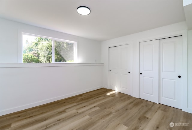 unfurnished bedroom featuring multiple closets and light wood-type flooring