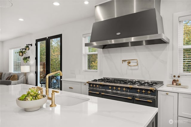 kitchen featuring backsplash, light stone countertops, sink, and wall chimney range hood