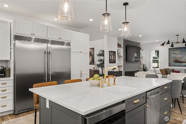 kitchen featuring pendant lighting, built in refrigerator, light stone counters, a kitchen bar, and white cabinetry