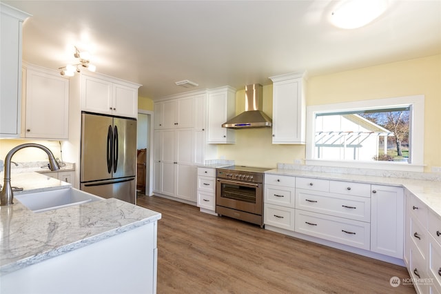 kitchen with sink, wall chimney range hood, wood-type flooring, white cabinets, and appliances with stainless steel finishes