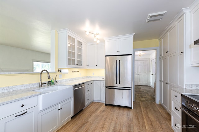 kitchen with white cabinets, sink, light wood-type flooring, light stone counters, and stainless steel appliances