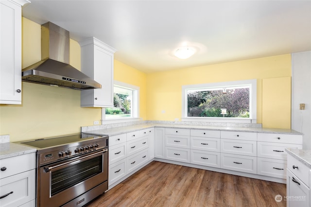 kitchen with light stone countertops, light wood-type flooring, wall chimney range hood, high end stainless steel range, and white cabinetry