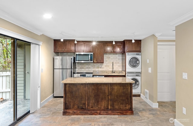 kitchen featuring sink, stacked washer / dryer, crown molding, a kitchen island, and appliances with stainless steel finishes