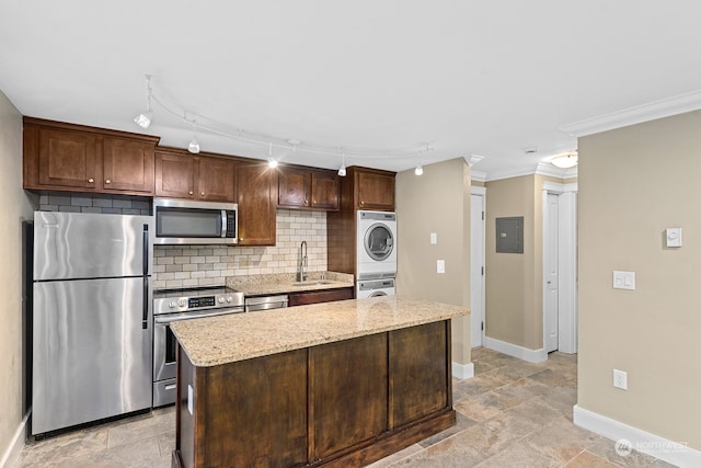 kitchen with sink, stacked washer / dryer, appliances with stainless steel finishes, a kitchen island, and ornamental molding