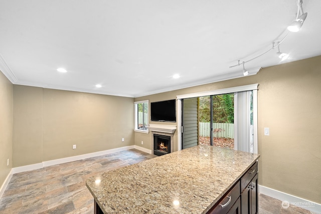 kitchen with dark brown cabinetry, a center island, light stone counters, and crown molding