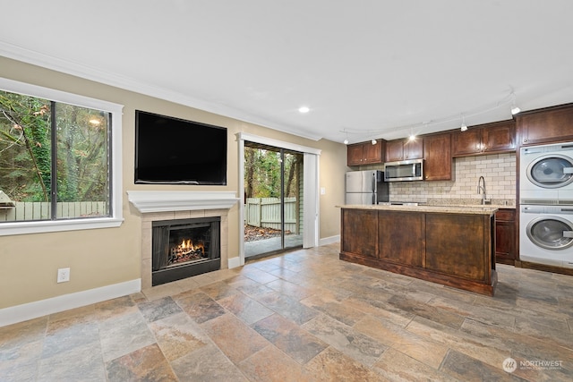 kitchen featuring decorative backsplash, ornamental molding, stainless steel appliances, a fireplace, and stacked washer and dryer