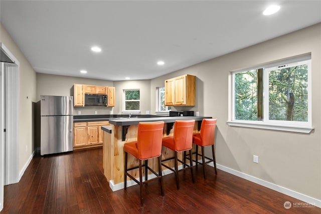 kitchen with light brown cabinets, dark wood-type flooring, kitchen peninsula, stainless steel fridge, and a kitchen bar