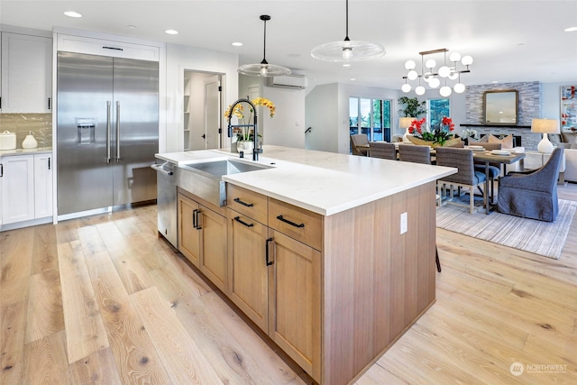 kitchen with sink, hanging light fixtures, stainless steel appliances, light hardwood / wood-style flooring, and a center island with sink