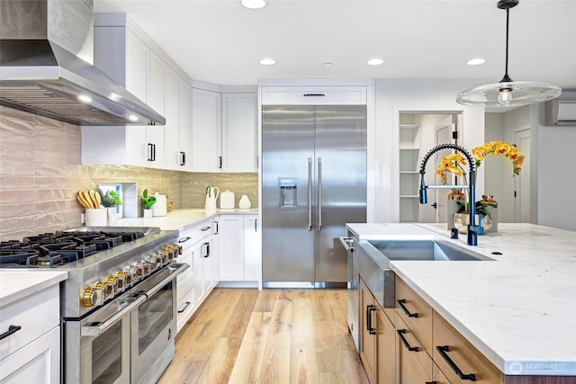 kitchen featuring white cabinetry, high quality appliances, wall chimney exhaust hood, and hanging light fixtures