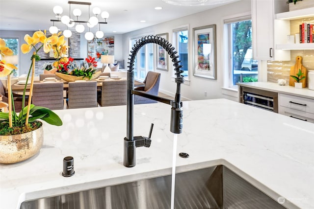 details with white cabinetry, pendant lighting, light stone counters, and a notable chandelier