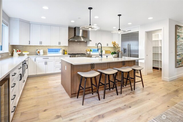 kitchen featuring white cabinetry, a kitchen island with sink, decorative light fixtures, and wall chimney range hood