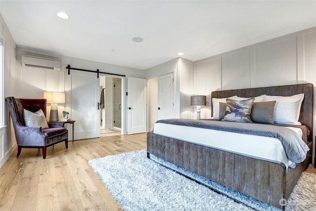 bedroom with a barn door, light hardwood / wood-style flooring, and a wall mounted AC