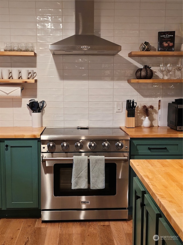 kitchen with high end range, green cabinetry, light hardwood / wood-style flooring, wall chimney exhaust hood, and butcher block countertops