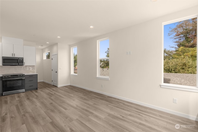 kitchen with light wood-style floors, white cabinets, light countertops, decorative backsplash, and electric range oven