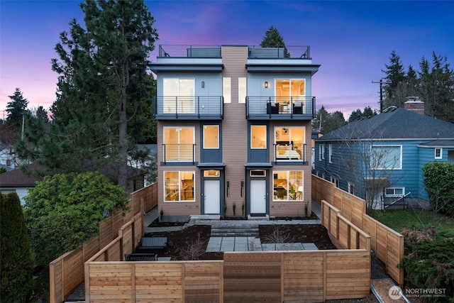 back of property at dusk featuring a fenced backyard and a balcony