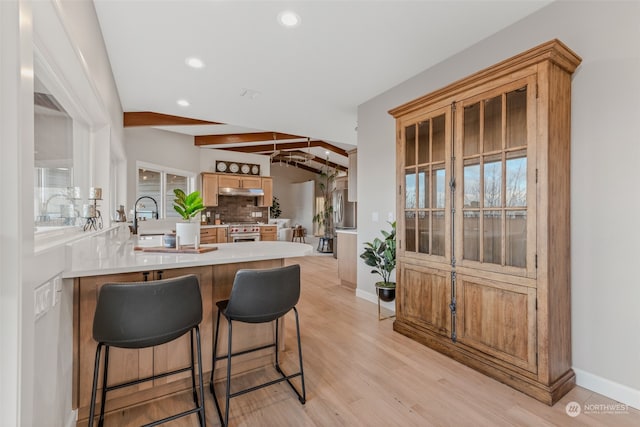 kitchen featuring vaulted ceiling with beams, a healthy amount of sunlight, high end stainless steel range oven, and light hardwood / wood-style floors