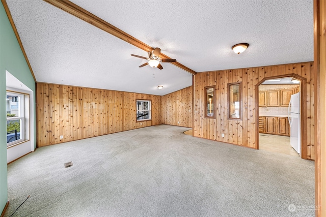 unfurnished living room with lofted ceiling with beams, light colored carpet, ceiling fan, and wood walls