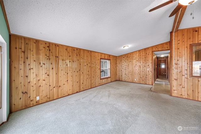 unfurnished living room featuring ceiling fan, wood walls, light colored carpet, a textured ceiling, and lofted ceiling