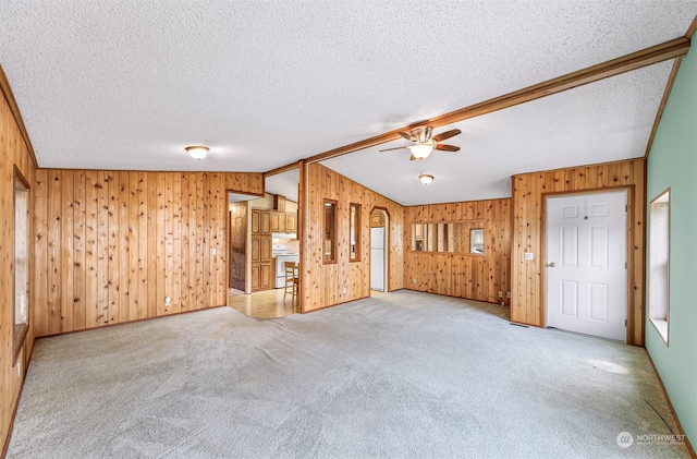 interior space with a textured ceiling, wooden walls, ceiling fan, and lofted ceiling