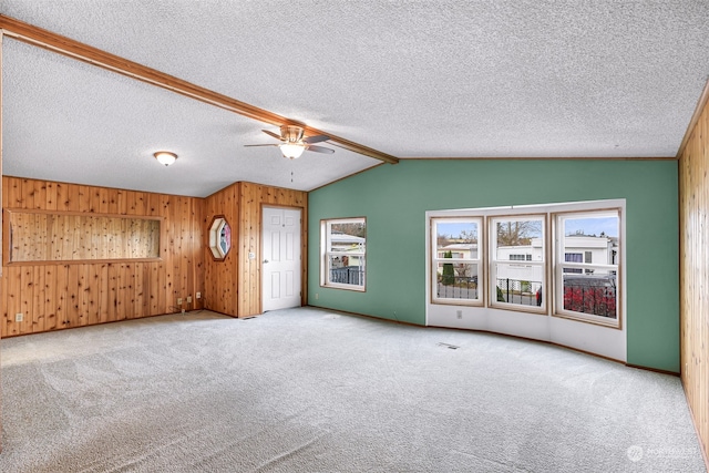 unfurnished living room with ceiling fan, wood walls, carpet floors, and a textured ceiling