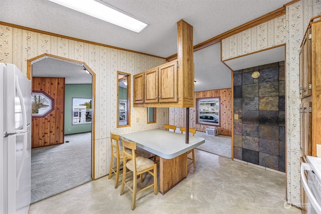 kitchen with a textured ceiling, white appliances, light colored carpet, crown molding, and a breakfast bar area