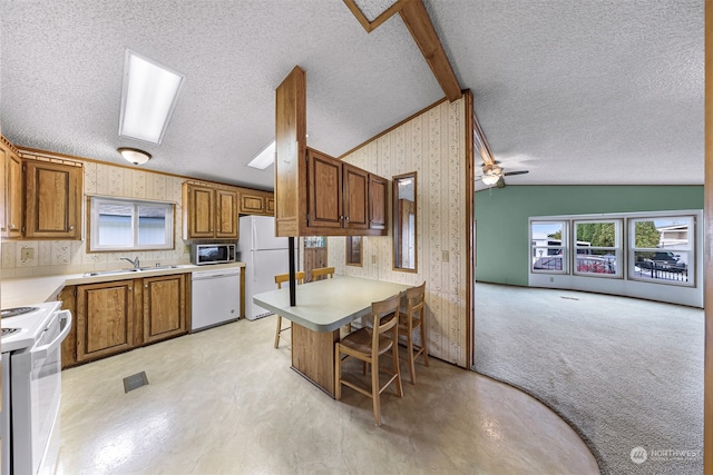 kitchen with white appliances, a kitchen breakfast bar, vaulted ceiling with skylight, ceiling fan, and a textured ceiling