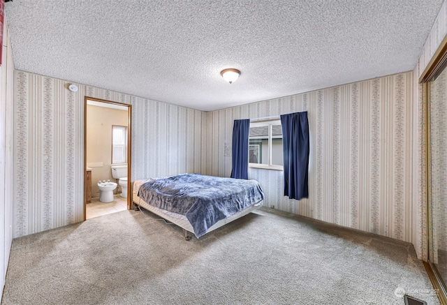 carpeted bedroom featuring ensuite bathroom and a textured ceiling