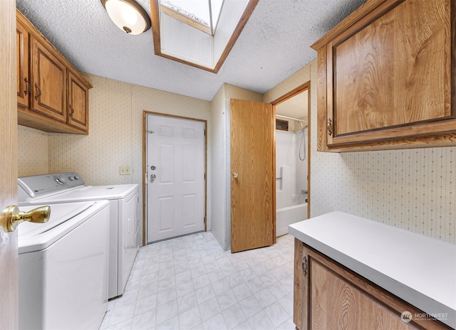 laundry area featuring cabinets, washing machine and dryer, a textured ceiling, and a skylight