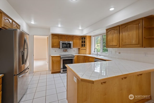 kitchen with sink, stainless steel appliances, backsplash, kitchen peninsula, and tile countertops