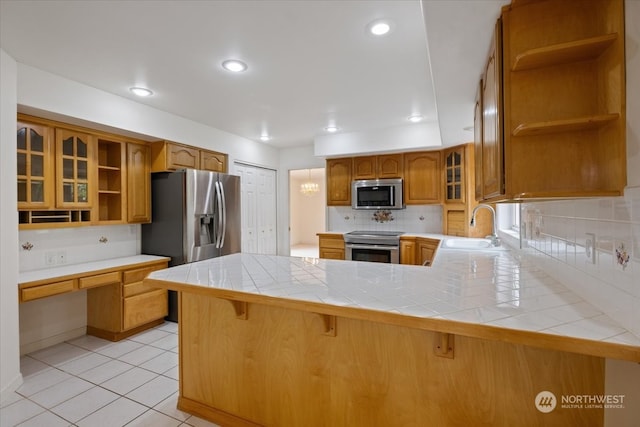 kitchen featuring tile counters, tasteful backsplash, kitchen peninsula, a breakfast bar area, and appliances with stainless steel finishes