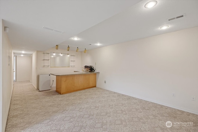 kitchen with light brown cabinets, kitchen peninsula, light carpet, and track lighting