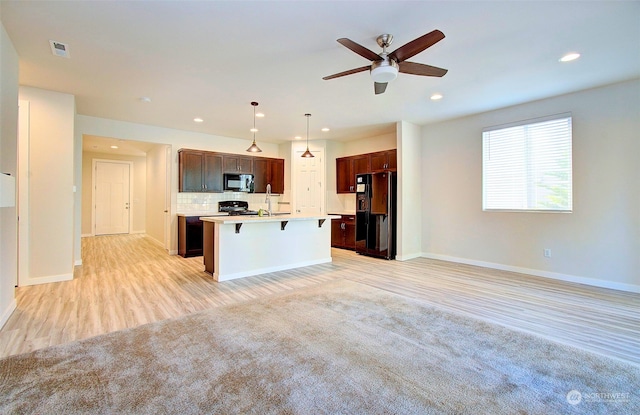 kitchen featuring a kitchen island with sink, a kitchen breakfast bar, black fridge, hanging light fixtures, and decorative backsplash