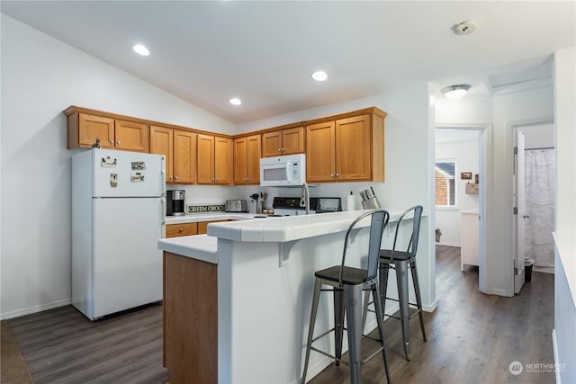 kitchen featuring dark hardwood / wood-style flooring, tile countertops, lofted ceiling, white appliances, and a kitchen bar