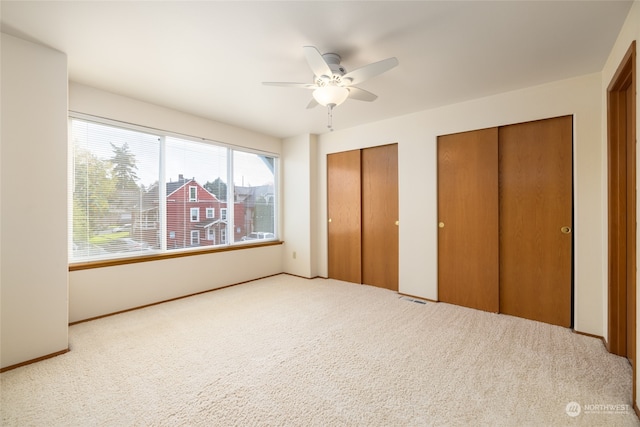 unfurnished bedroom with multiple closets, carpet floors, and ceiling fan