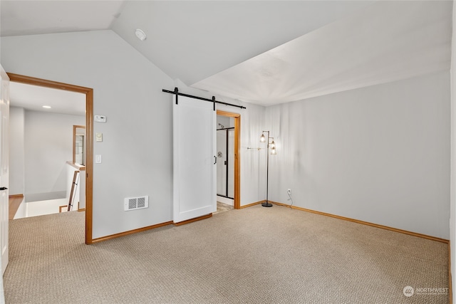 empty room with carpet flooring, a barn door, and lofted ceiling