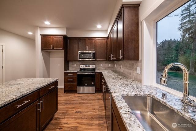 kitchen with decorative backsplash, light stone counters, stainless steel appliances, sink, and hardwood / wood-style floors