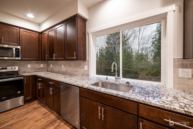 kitchen with sink, stainless steel appliances, light stone counters, dark brown cabinets, and light wood-type flooring