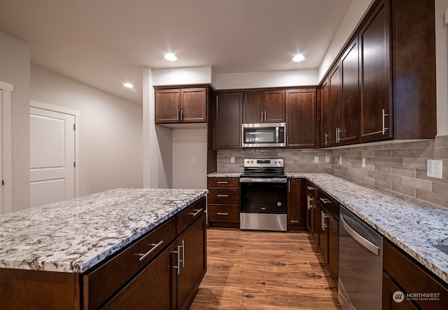 kitchen featuring light wood-type flooring, tasteful backsplash, light stone counters, stainless steel appliances, and a kitchen island