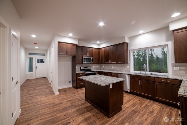 kitchen with a center island, sink, light stone counters, wood-type flooring, and appliances with stainless steel finishes