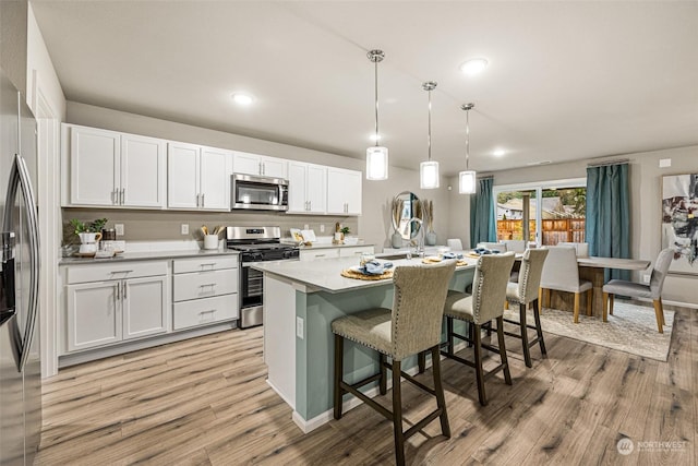 kitchen featuring a breakfast bar area, hanging light fixtures, appliances with stainless steel finishes, an island with sink, and white cabinets