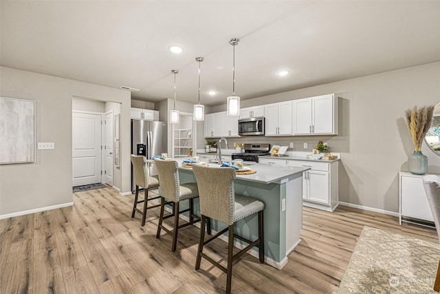 kitchen with a center island with sink, appliances with stainless steel finishes, pendant lighting, light hardwood / wood-style floors, and white cabinets