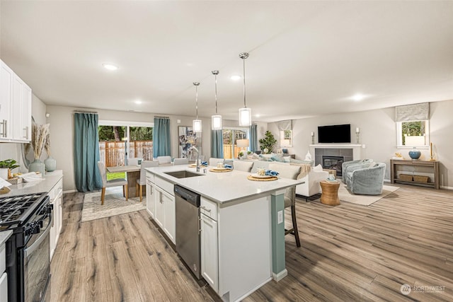 kitchen featuring sink, a center island with sink, black gas stove, dishwasher, and white cabinets