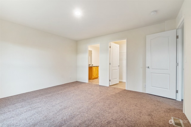 unfurnished bedroom with light carpet, a walk in closet, ensuite bath, and a closet