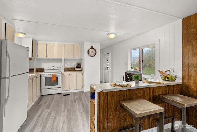 kitchen featuring kitchen peninsula, a kitchen bar, white appliances, and light hardwood / wood-style flooring