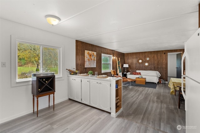 kitchen with white cabinets, light hardwood / wood-style floors, a healthy amount of sunlight, and wooden walls