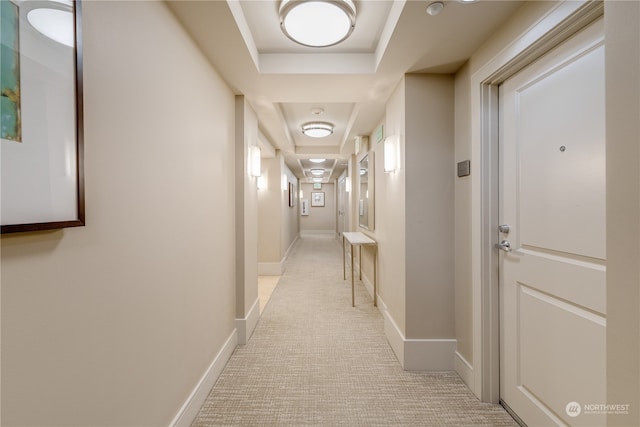 hallway featuring light colored carpet and a tray ceiling