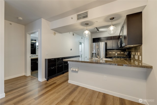 kitchen featuring backsplash, kitchen peninsula, pendant lighting, light hardwood / wood-style floors, and appliances with stainless steel finishes