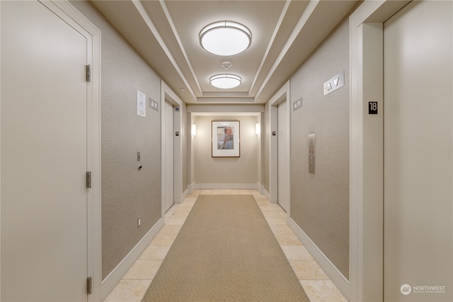 hallway featuring a raised ceiling, elevator, and light tile patterned floors