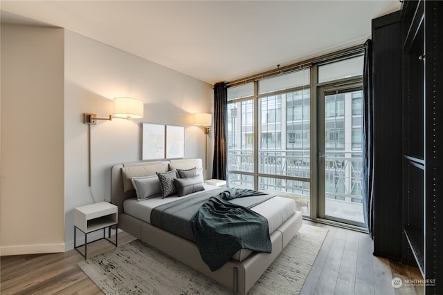 bedroom with access to exterior, hardwood / wood-style floors, and a wall of windows