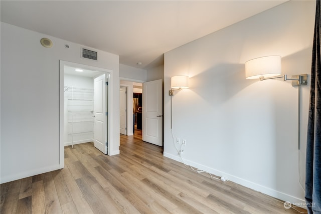 unfurnished bedroom featuring a walk in closet, a closet, and light hardwood / wood-style flooring